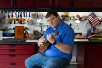 A man sitting on a stool by a workbench, playing a ukulele