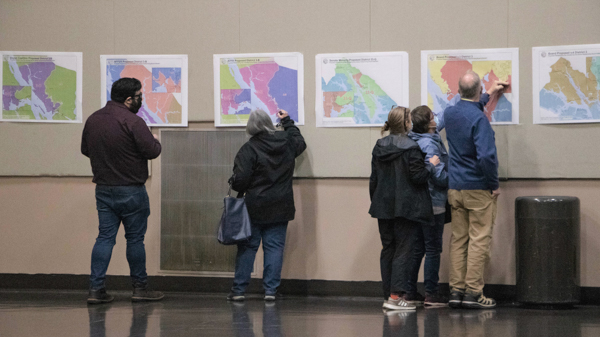 People in a large room looking at different maps on a wall
