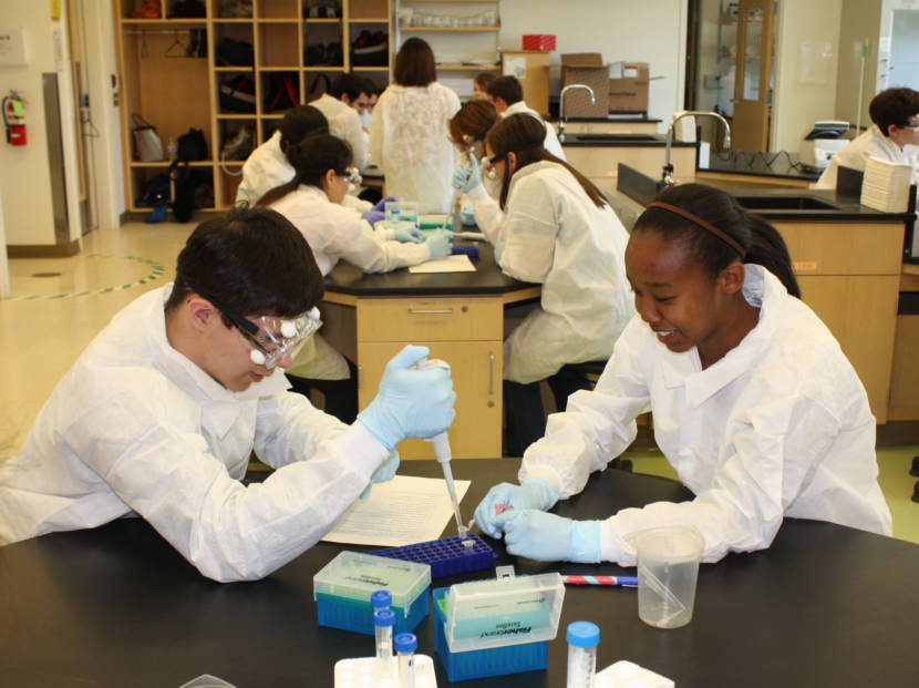 Students in lab coats seated around tables