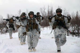 A group of soldiers wearing winter camouflage and bunny boots marching in the snow