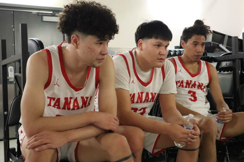 Three high school basketball players in uniform, sitting next to each other
