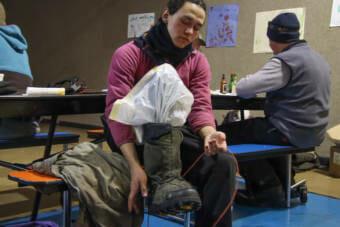 A woman in a purple outer layer ties a boot while sitting on a cafeteria bench