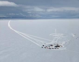 An aerial view of a crowd of people with snowmachines gathered in a remote spot on a frozen lake