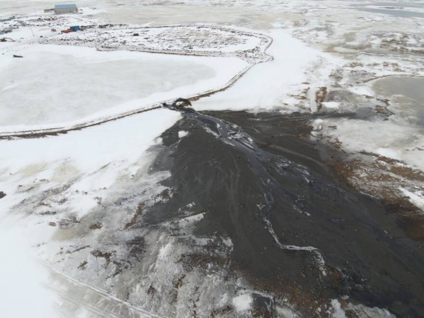 An aerial photo of a brown area downhill of a breach in the wall of an ice-covered lagoon