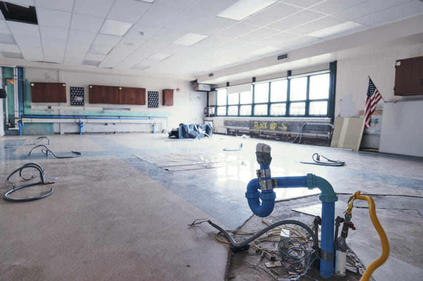 An empty classroom with a damaged floor and all of the furniture removed