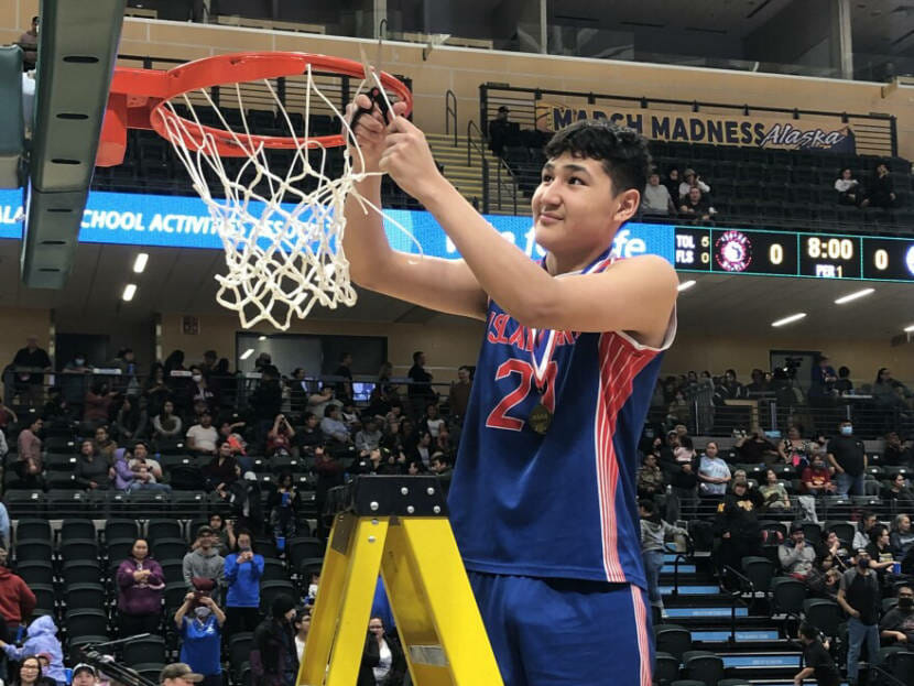 A high school basketball player stands on a stepladder to cut down a net