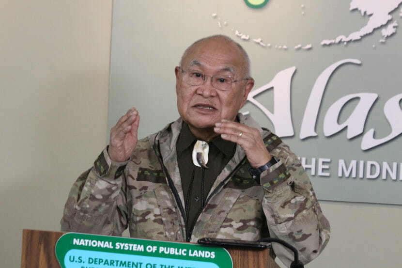 A man in a camouflage jacket speaks from behind a lectern