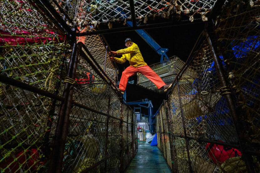 A fisherman on top two stacks of crab pots in the dark