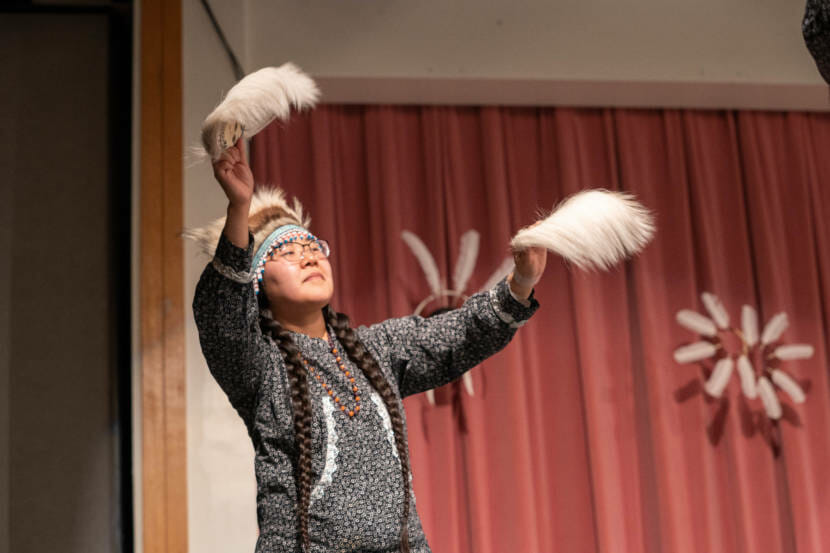 A single dancer, with arms outstretched, holding feathers in both hands