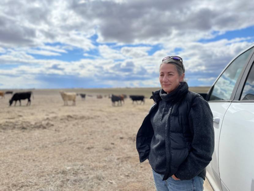 A portrait of a woman in work clothes with cattle behind her