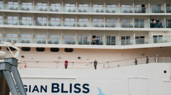 The side of a large cruise ship, with passengers visible on walkways