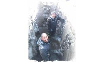 Two men stand at the bottom of a freshly dug grave