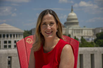 A woman in a red dress sitting in a red Adirondack chair with the U.S. Capitol in the background