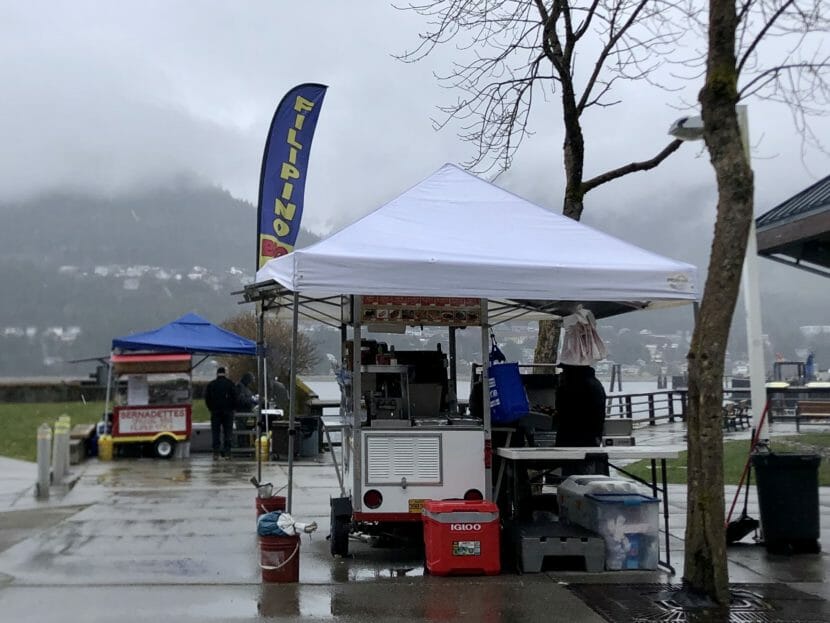 A food stand in Juneau's Marine Park is a collection of tables, grills and coolers under a white tent. A vertical banner says "Filipino BBQ" in blue, yellow and red -- the colors of the Philippines flag.