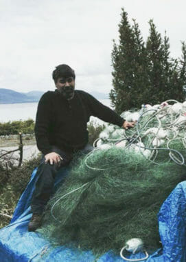 A man sits by a pile of fishing nets and floats