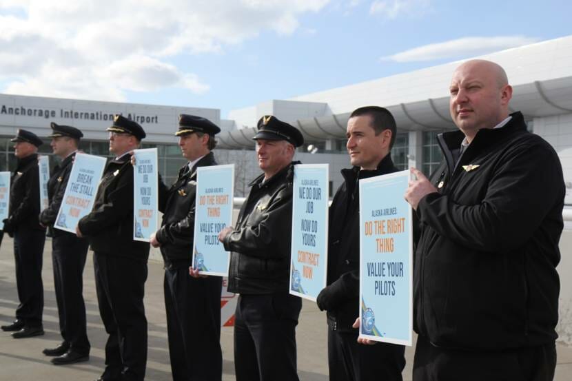 A row of pilots holding picket signs with slogans like "Break the stall: contract now"