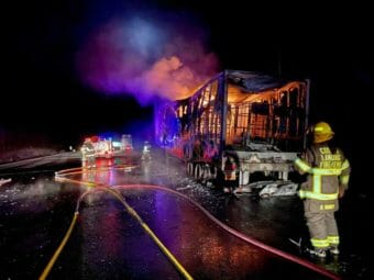 Firemen stand near a burned-out tractor trailer that is still on fire