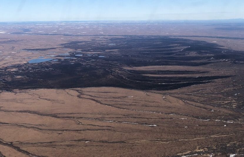 An aerial view of a brown tundra landscape with a large burned area in the middle