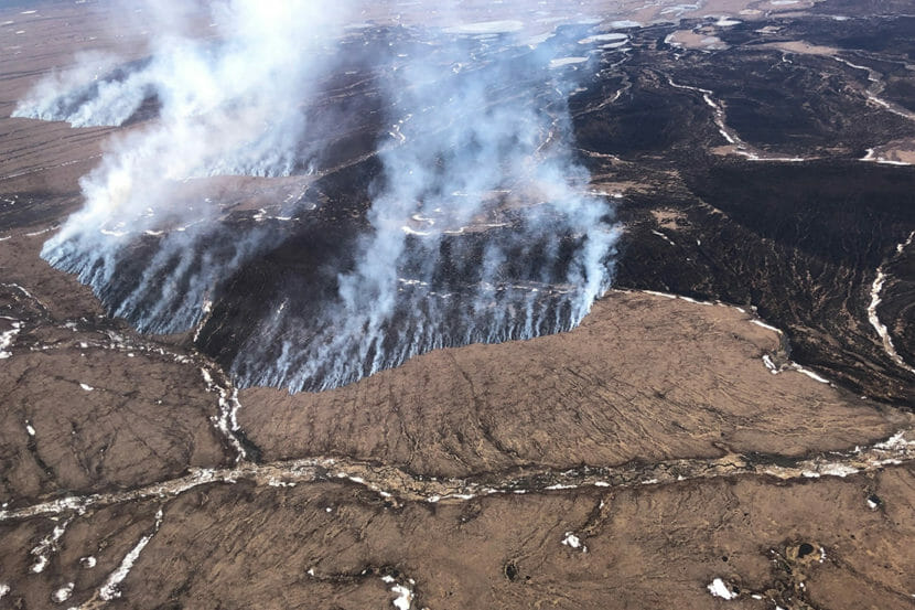 An aerial photo of a large fire burning in brown tundra