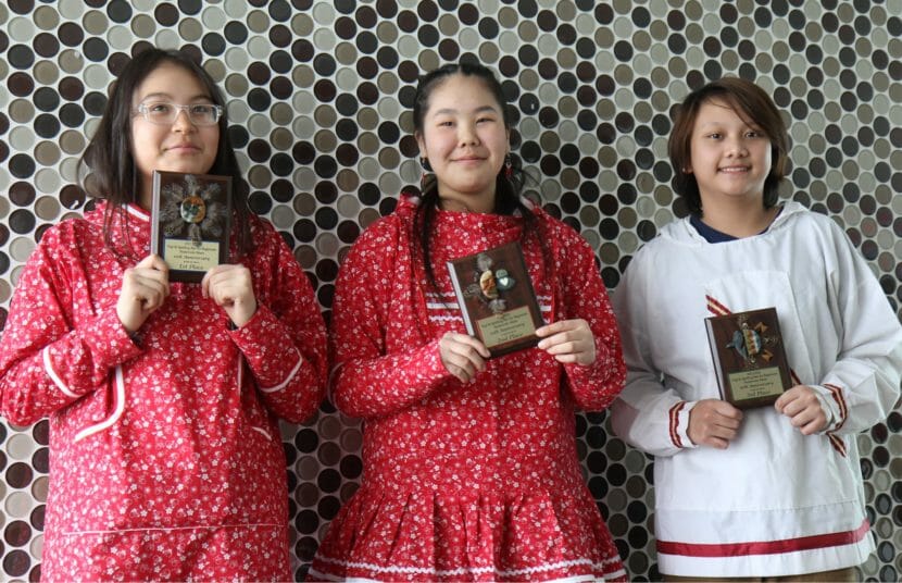 Three children pose while holding their spelling bee plaques