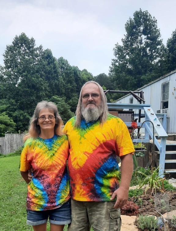 A couple wearing tie-die stand outside a home