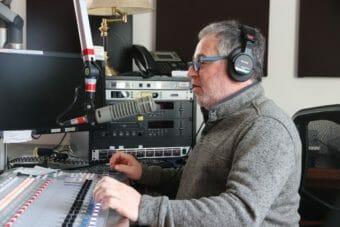 A man wearing headphones and speaking into a mic in a radio studio
