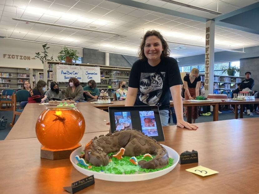 Thunder Mountain High School student Abigail Sparks poses with the cake she made for her final project. The creation was part of the Great Literature Bake-Off in the TMHS library on Tuesday, May 24, 2022.