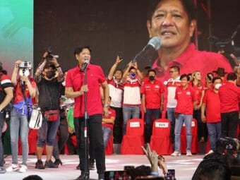 Ferdinand "Bongbong" Marcos Jr. speaks on a stage with supporters behind him