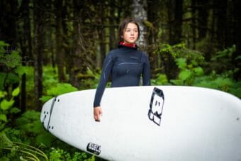 A young woman carrying a surfboard in a forest