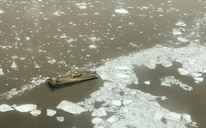 A barge with a loader on it surrounded by chunks of ice on a river