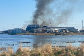 Smoke billowing from a group of buildings seen from across a body of water