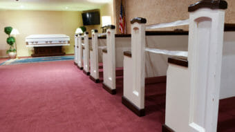 A photo looking down the aisle of a funeral home at a casket