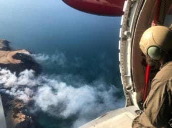 A firefighter looking out of the side of an airplane at smoke on an island