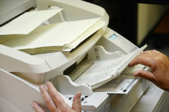 A pair of hands guiding ballots into a beige scanner