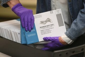Gloved hands holding a box full of mail-in ballots