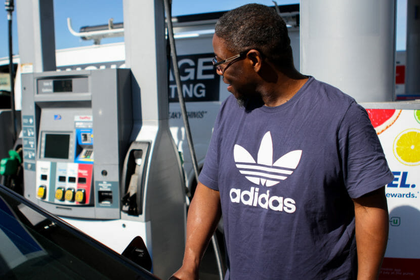 A man in a t-shirt pumping gas on a sunny day