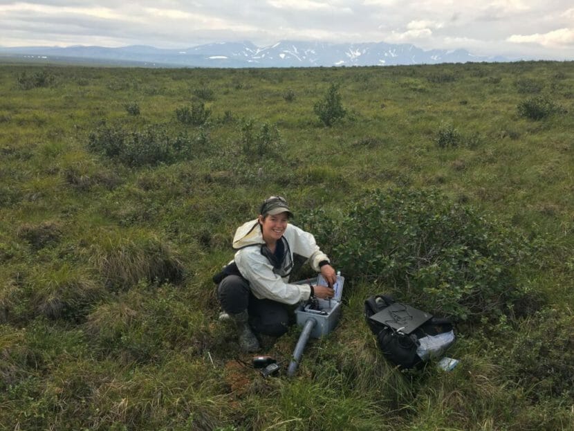 A woman sits on the tundra with miscellaneous scientific equipment
