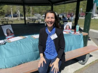 Mary Peltola smiles from the bench of a picnic table set up as a campaign booth