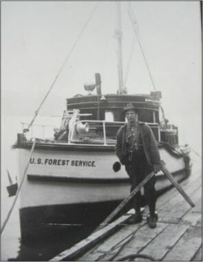 A black and white photo of a man standing next to a docked boat