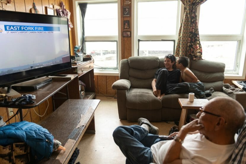 A family watches coverage of the fire in their living room as smoke is visible outside through their windows