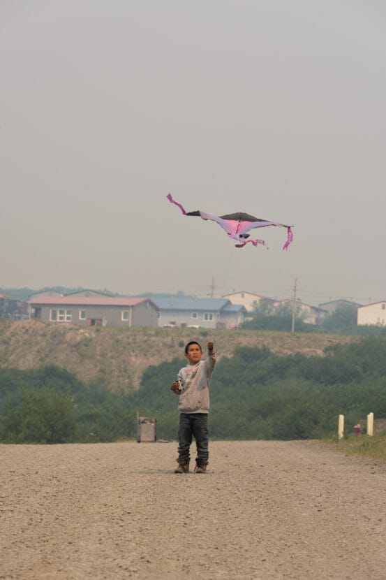 A boy flies a kite on a dirt road in extremely smoky skies