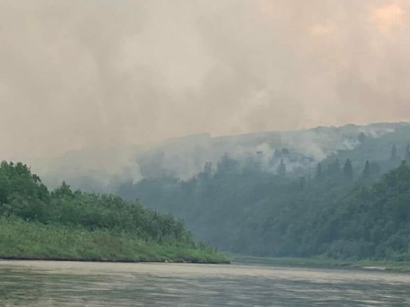 A view looking down a river at smoky forest with an orange glow behind it