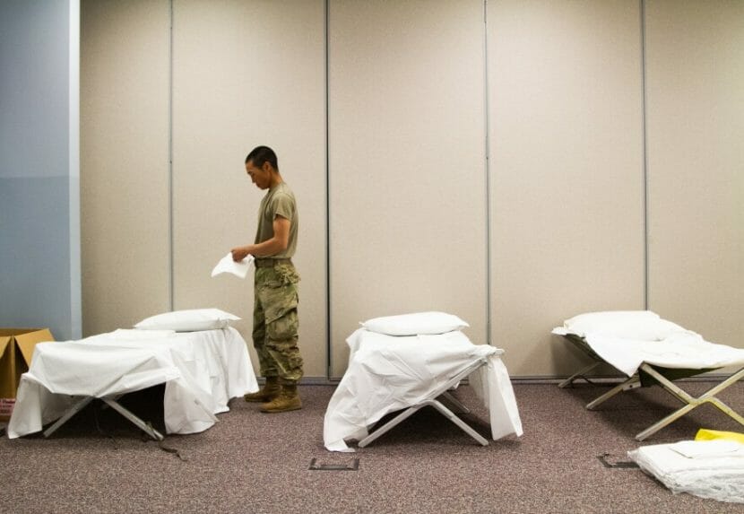 A man in uniform standing in a room full of white, freshly made cots.