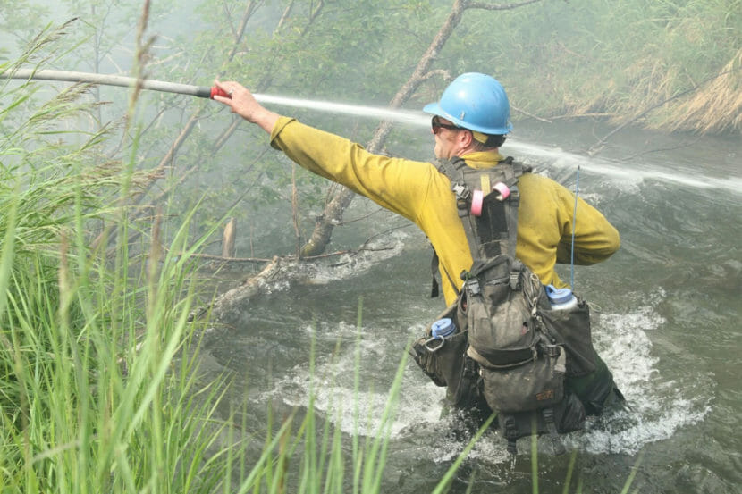 A firefighter standing in a stream and trying to manage a firehose