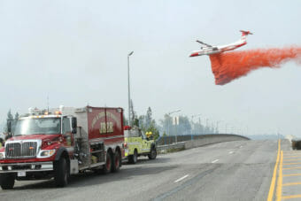 A tanker dropping a load of orange fire retardant in woods right next to an Anchorage road