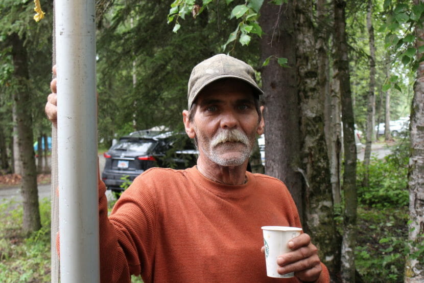 A man leans against a tree holding a cup of coffee