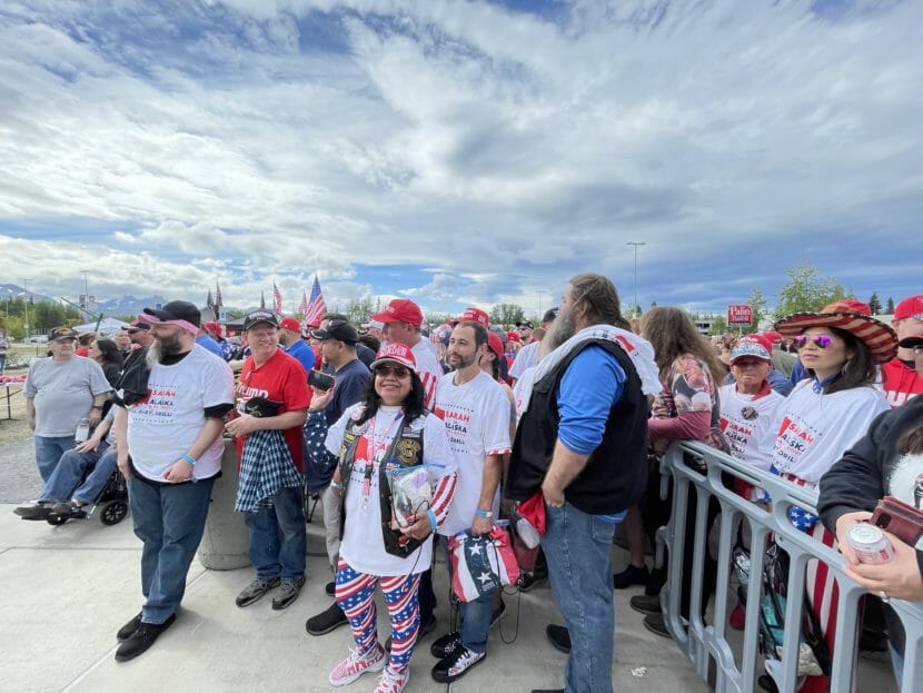 People dressed in red, white and blue stand by a crowd control barricade.