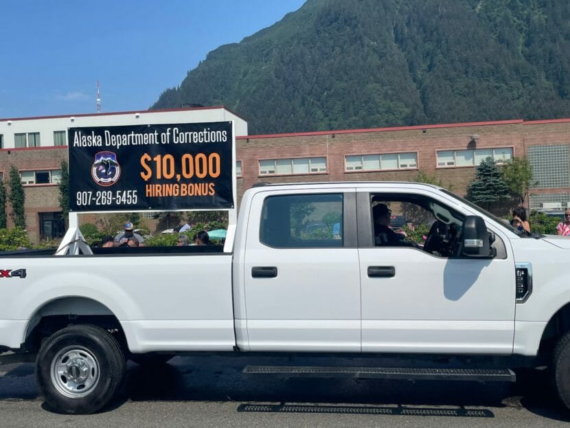 A white pickup truck with a sign mounted in the bed that reads "Alaska Department of Corrections $10,000 hiring bonus"