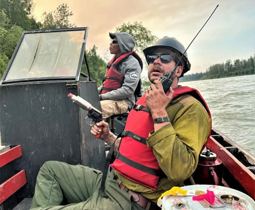 Two firefighters on a boat, one holding a flare gun