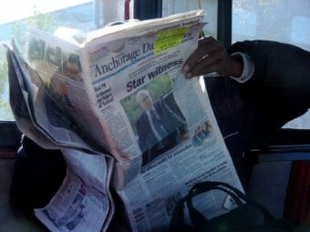 A man reading a newspaper on the bus
